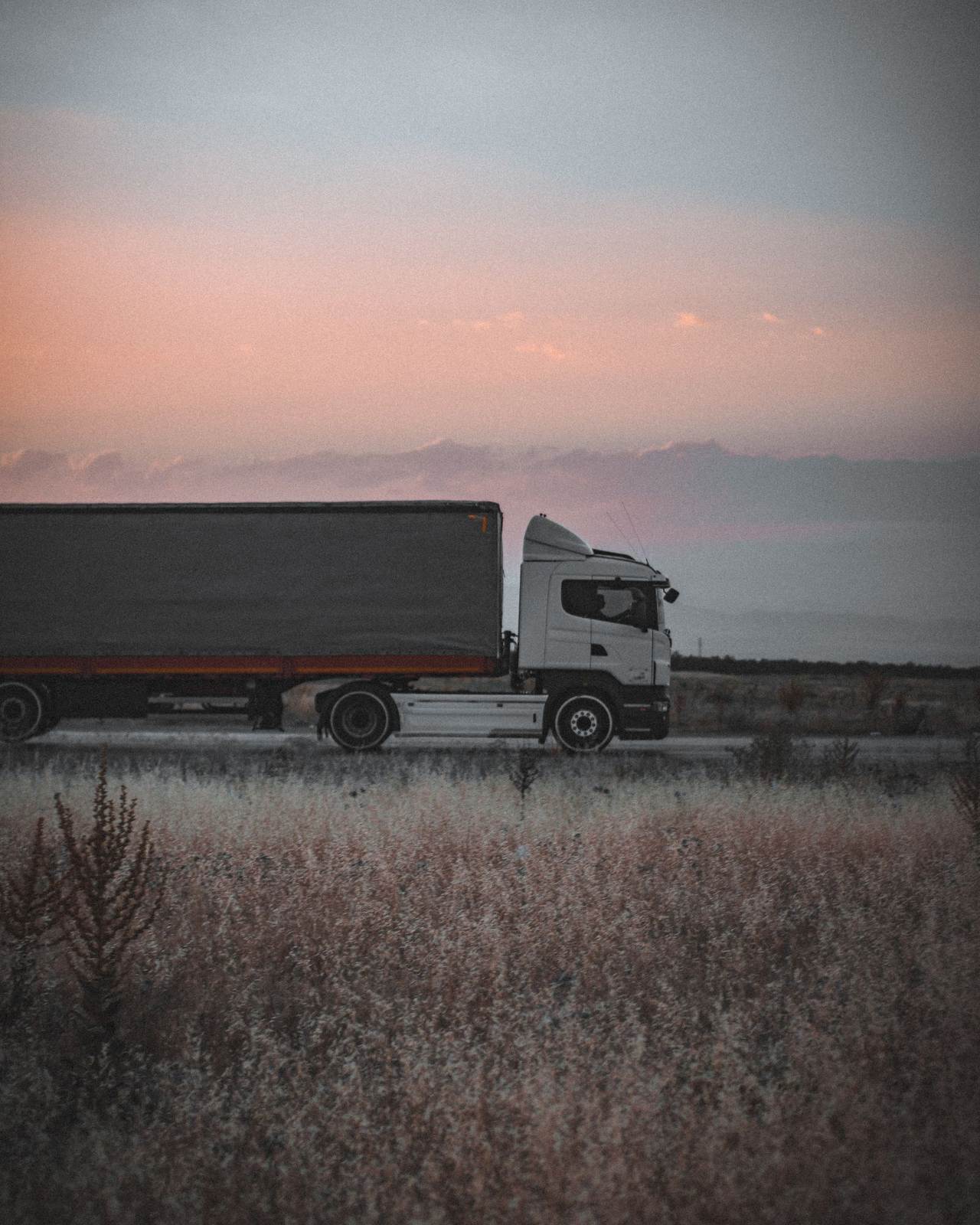 A cargo truck travels on a highway at sunset, surrounded by an open landscape, symbolizing logistics and transportation